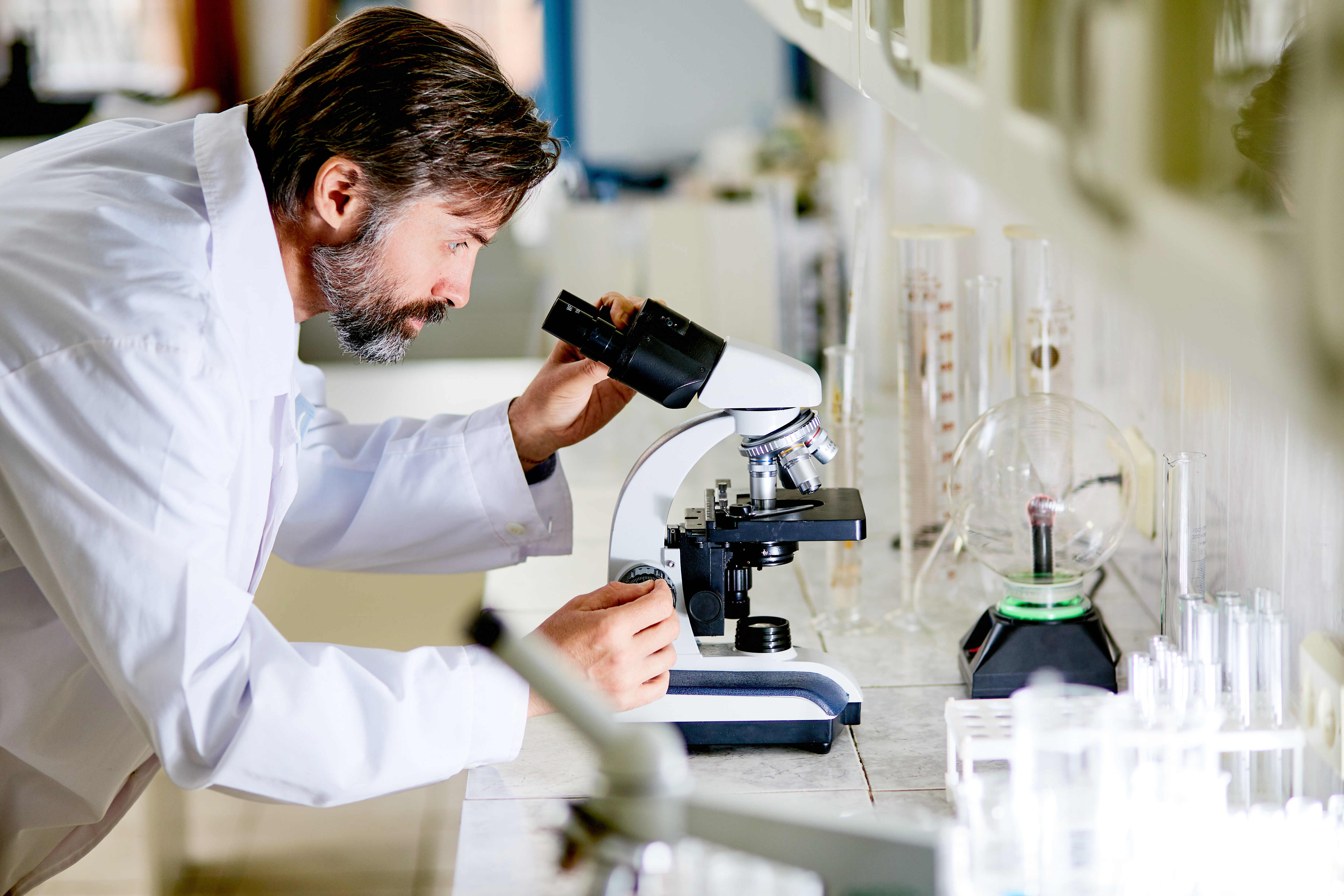 Mature scientist looking in microscope during chemical investigation in lab